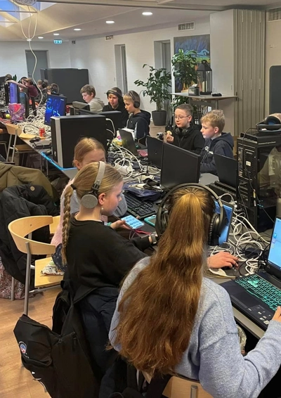 En masse unge ved at lang bord, hvorpå der står en masse computere og spille devices.